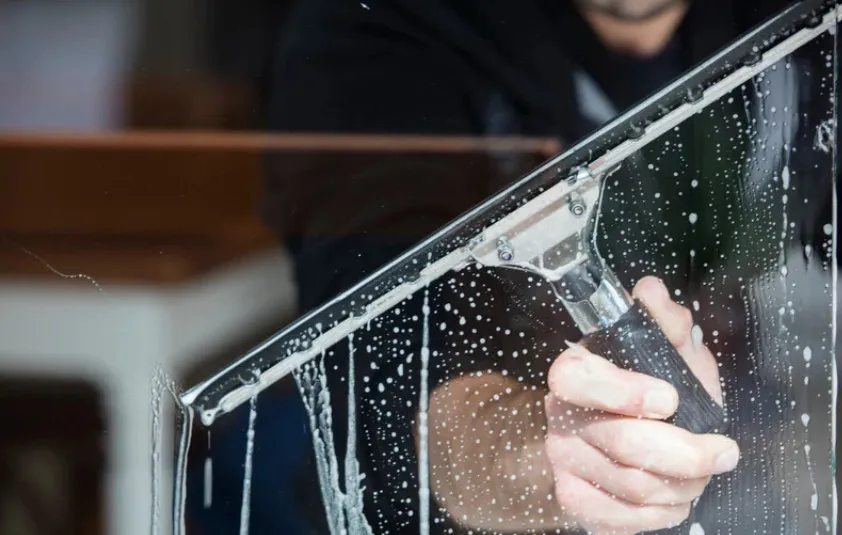 Person cleaning window with squeegee and soap bubbles.
